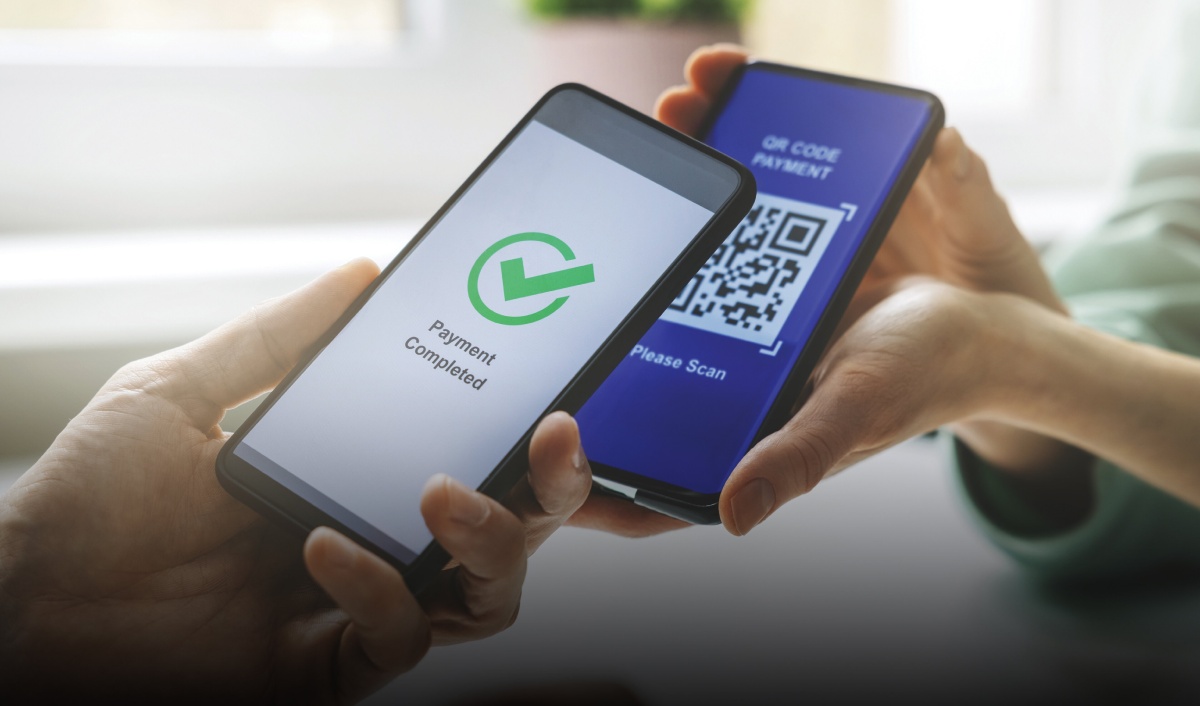 A village shopkeeper using UPI on a mobile phone with a QR code on display, cows and children in the background